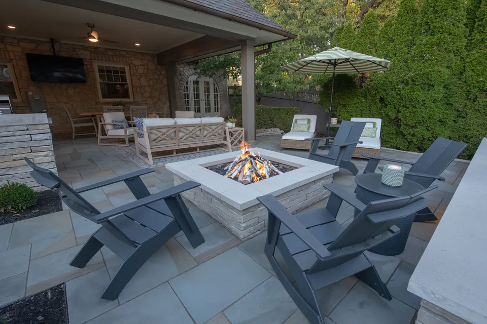 Rectangular gas firepit with stacked natural stone, limestone cap, ceramic gas logs, lounge chairs, and bluestone patio